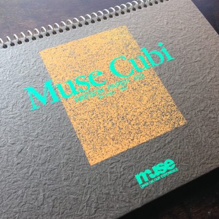 緑色で「Muse Cubi」というロゴが書かれたミニサイズの茶色いスケッチブックを撮影した写真。中にはクリーム色のワトソン紙が綴じられている。