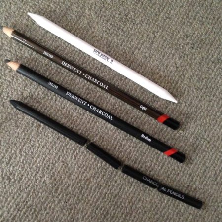 Derwentのチャコールペンシル（木炭鉛筆）（Mediumとlight）3本とholbeinの白い擦筆1本が灰色のカーペットの上に並んでいる