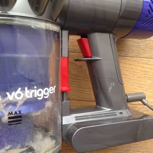 布団掃除機Dyson V6 Triggerの持ち手の部分を拡大して撮影した写真。電源オンオフを切り替える赤いボタンと「v6 trigger」と書かれた白いロゴが見えている