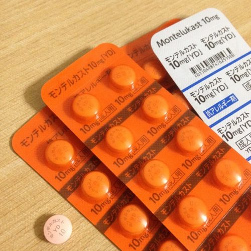 モンテルカスト10mgの錠剤を上から撮影した写真。オレンジ色のプラスチックパッケージに入れられた錠剤と、パッケージから取り出された薄いオレンジ色の錠剤が1粒写っている。