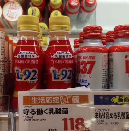 スーパーの陳列棚に、L-92乳酸菌ドリンクが展示されている様子。「守る働く乳酸菌 118円」と書かれた値札が貼られている。
