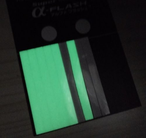 暗闇の中で超高輝度蓄光テープが「Super α-FLASH」が緑色の光を発している写真。蓄光テープは長方形型で、光も緑の長方形のように見える。